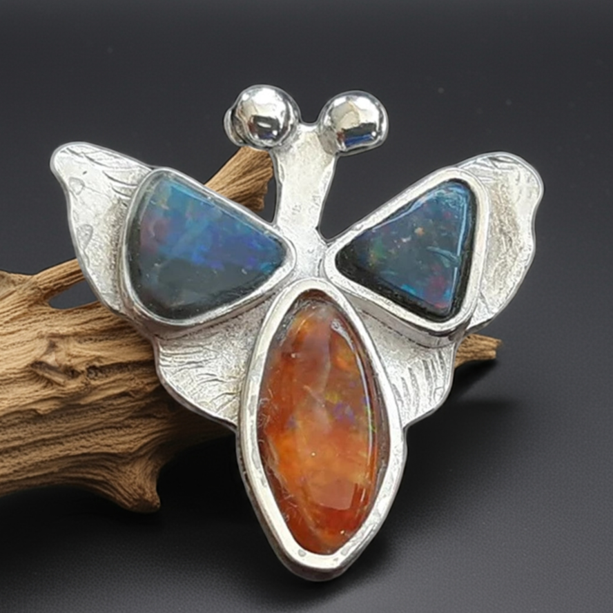 Butterfly-shaped silver brooch with blue and orange stones on a dark background